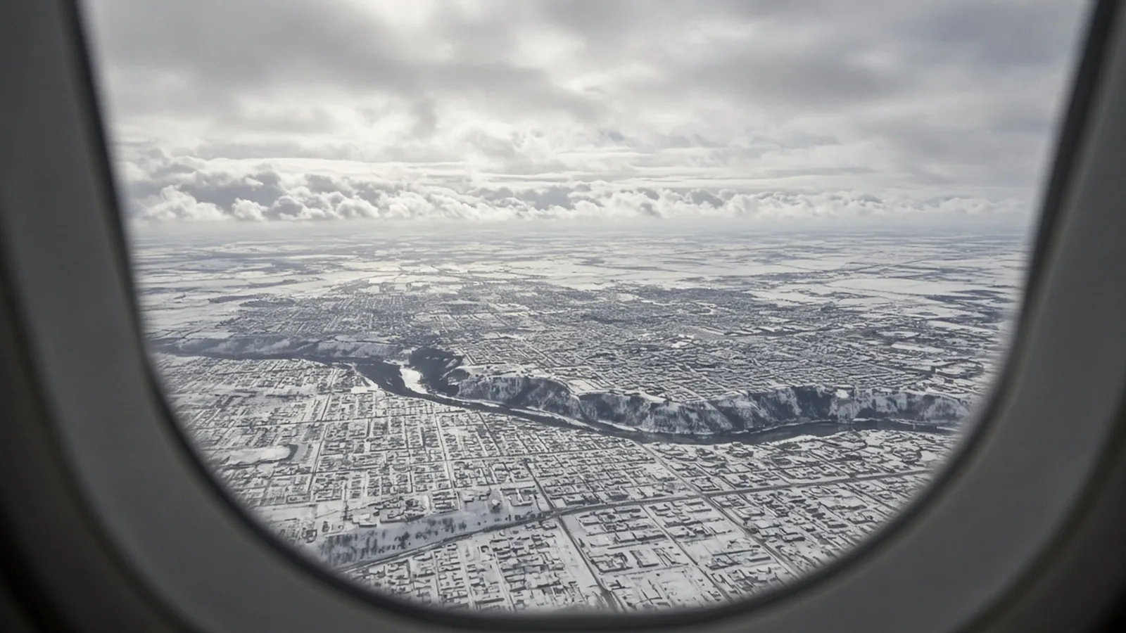 Airplane window over a snowy prairie city grid
